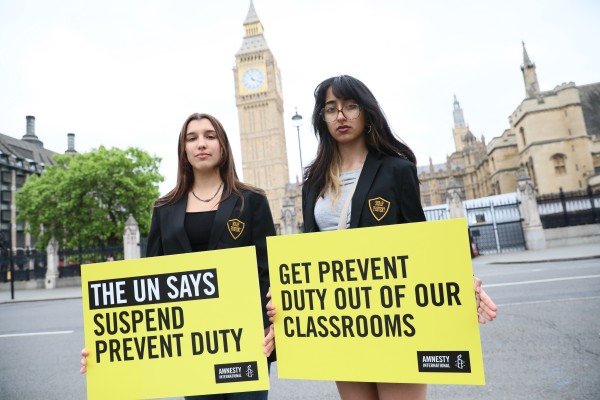 Image of two young people holding Amnesty placards reading "The UN says suspend Prevent Duty" and "Get Prevent Duty out of our classrooms".